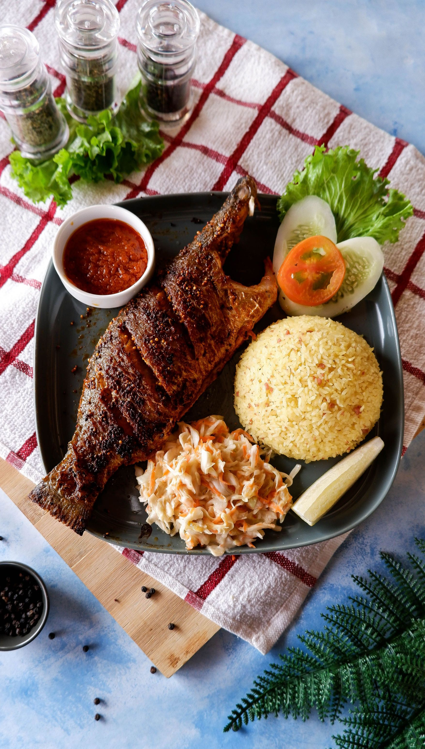 Grilled meat with rice, salad, sauce, and vegetables on a black plate on a checkered cloth