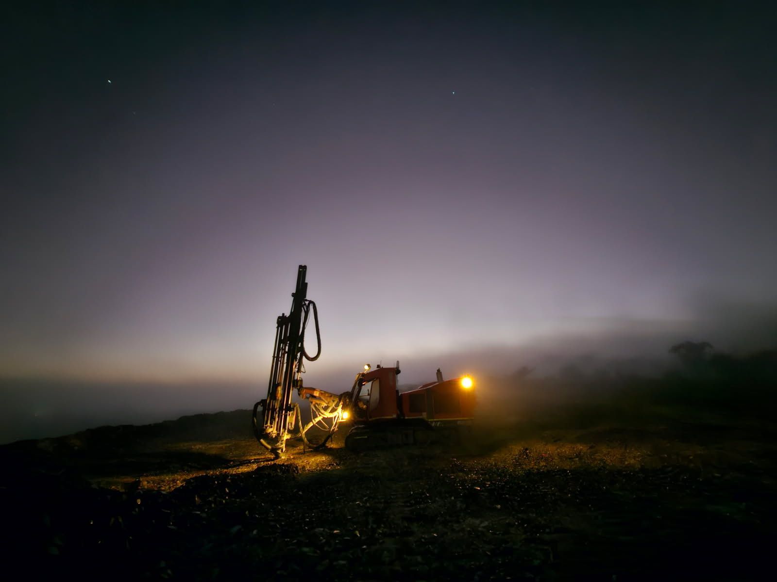 A yellow excavator is drilling a hole in the ground in a quarry.