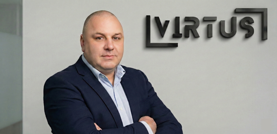 Roman in a navy blazer and light shirt stands with arms crossed against a light wall with a black Virtus company logo.