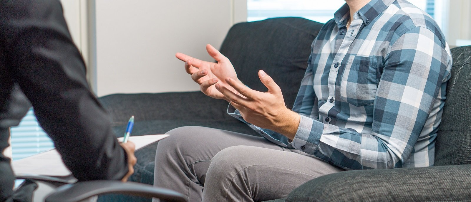 Un uomo è seduto su un divano e parla con un altro uomo.