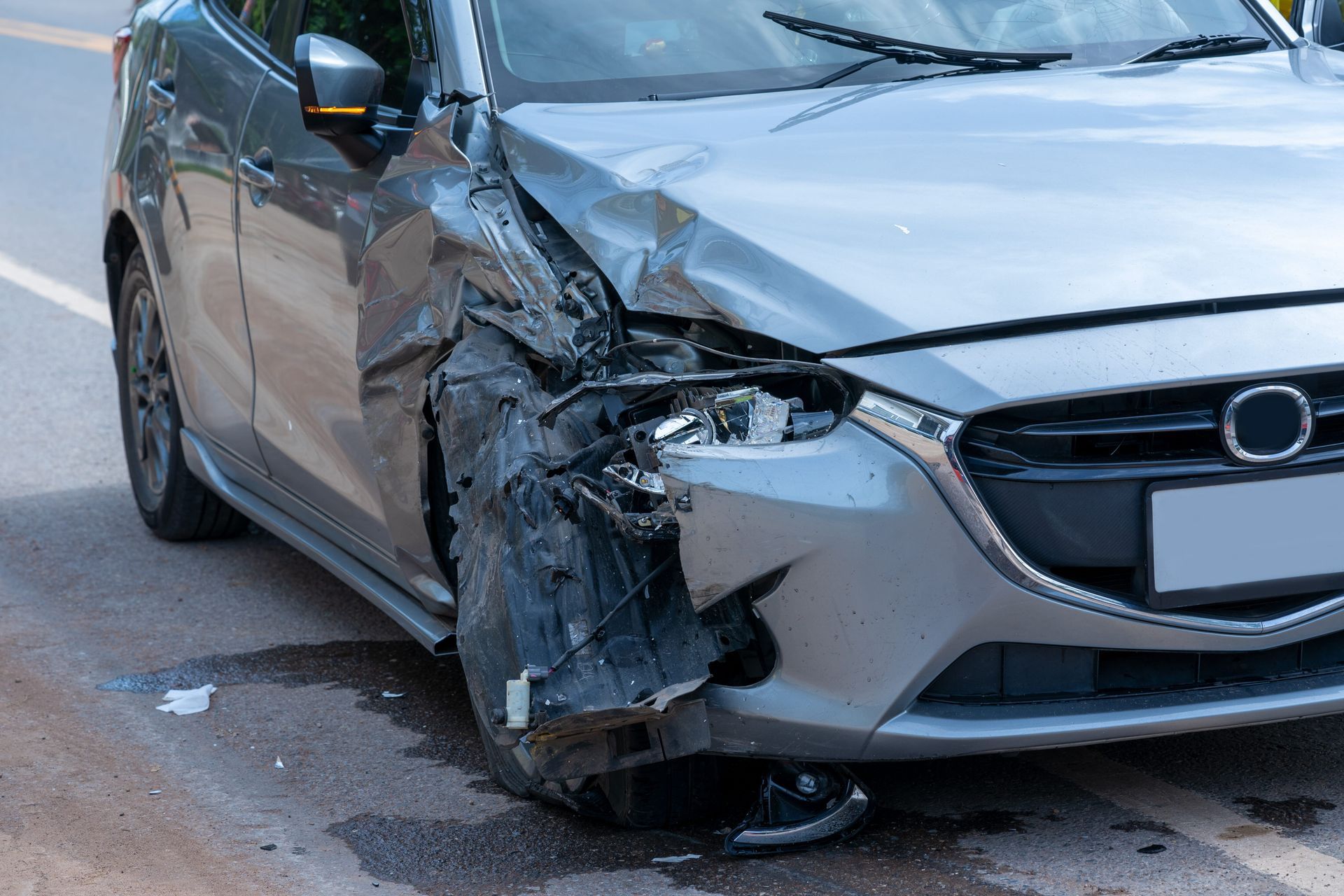 Front-left damage on a gray car after a collision, with a crushed bumper and crumpled fender on the road