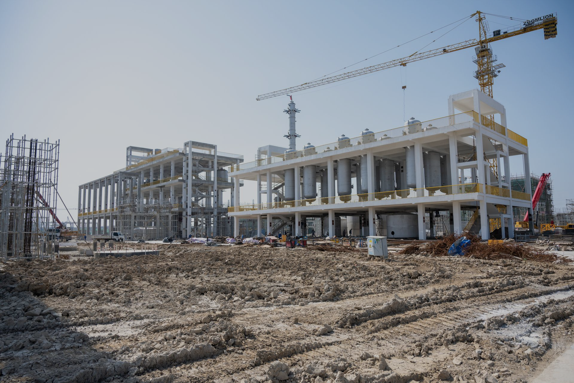 Cantiere con edifici in cemento, gru e terreno fangoso.