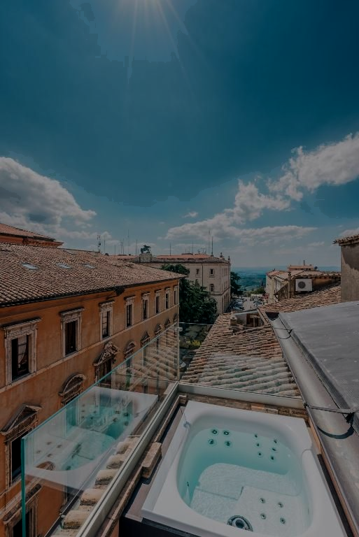 Jacuzzi sul tetto con vista sulla città sotto un cielo azzurro. Edifici con tetti in terracotta sullo sfondo.