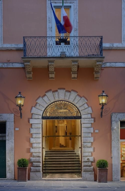 Un edificio con un balcone, un portale ad arco e una bandiera francese. Sera.