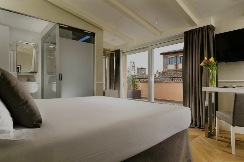 Camera da letto con letto, porta scorrevole in vetro che si apre su un balcone e bagno annesso.
