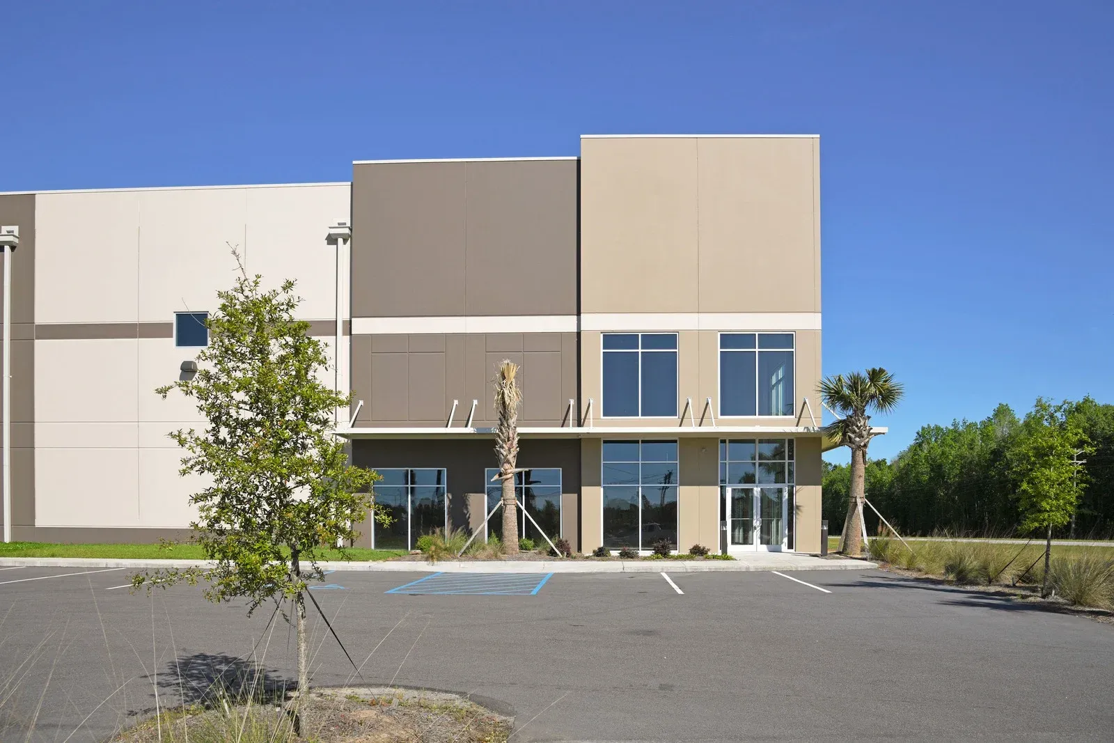 Modern industrial building with tan and brown facade, glass windows, and parking lot.
