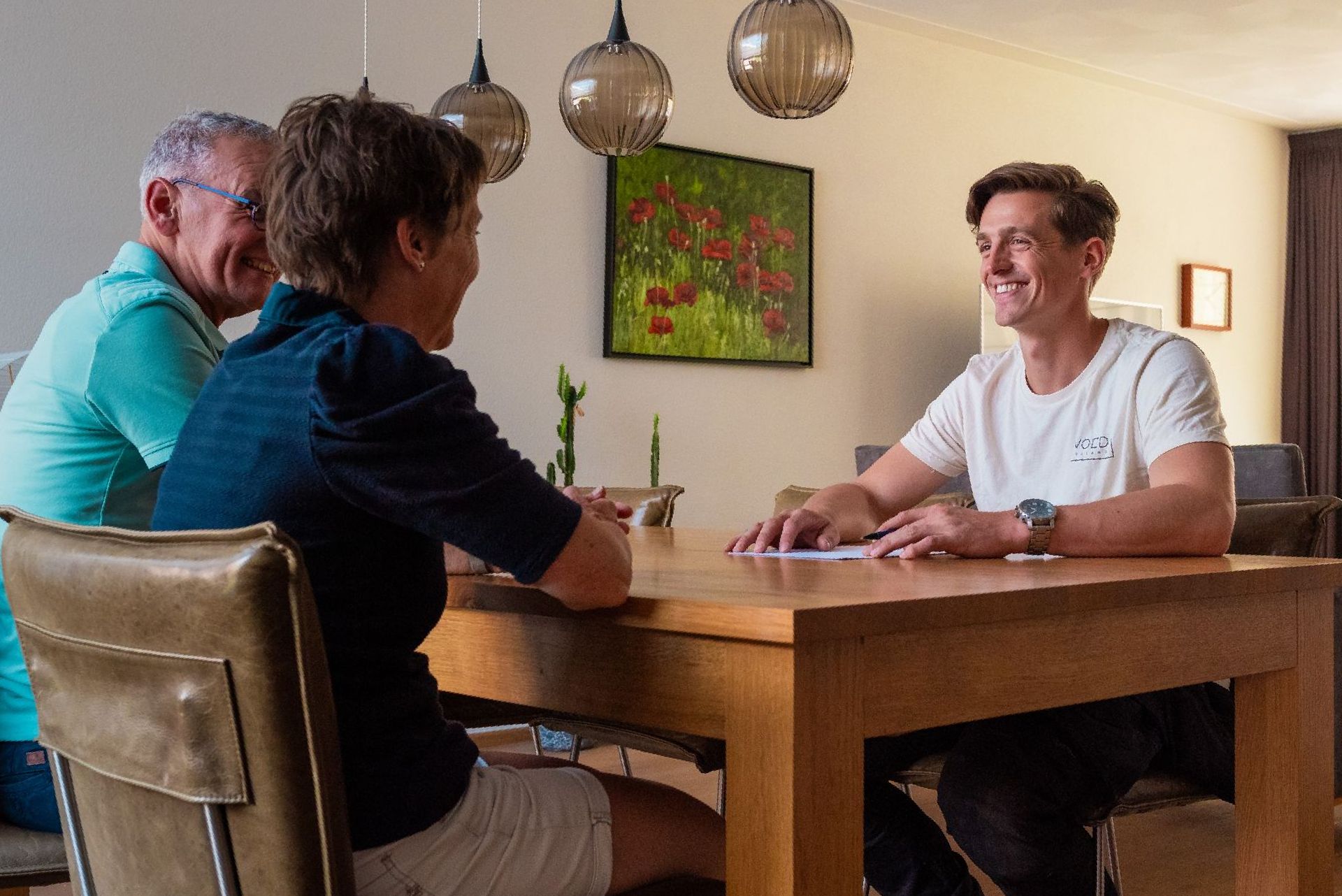 Een man zit met twee andere mensen aan een tafel.