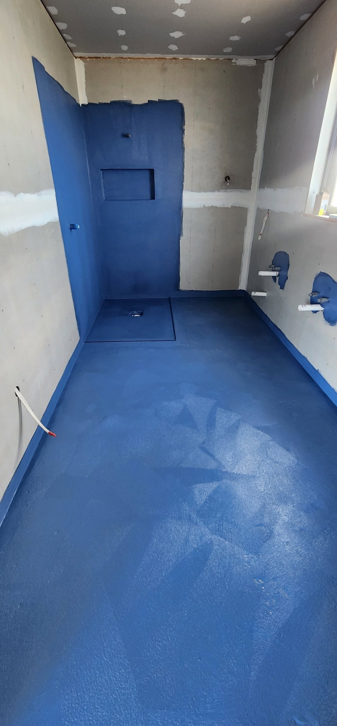 Small unfinished bathroom with blue waterproof flooring and wall panels, showing a shower area.