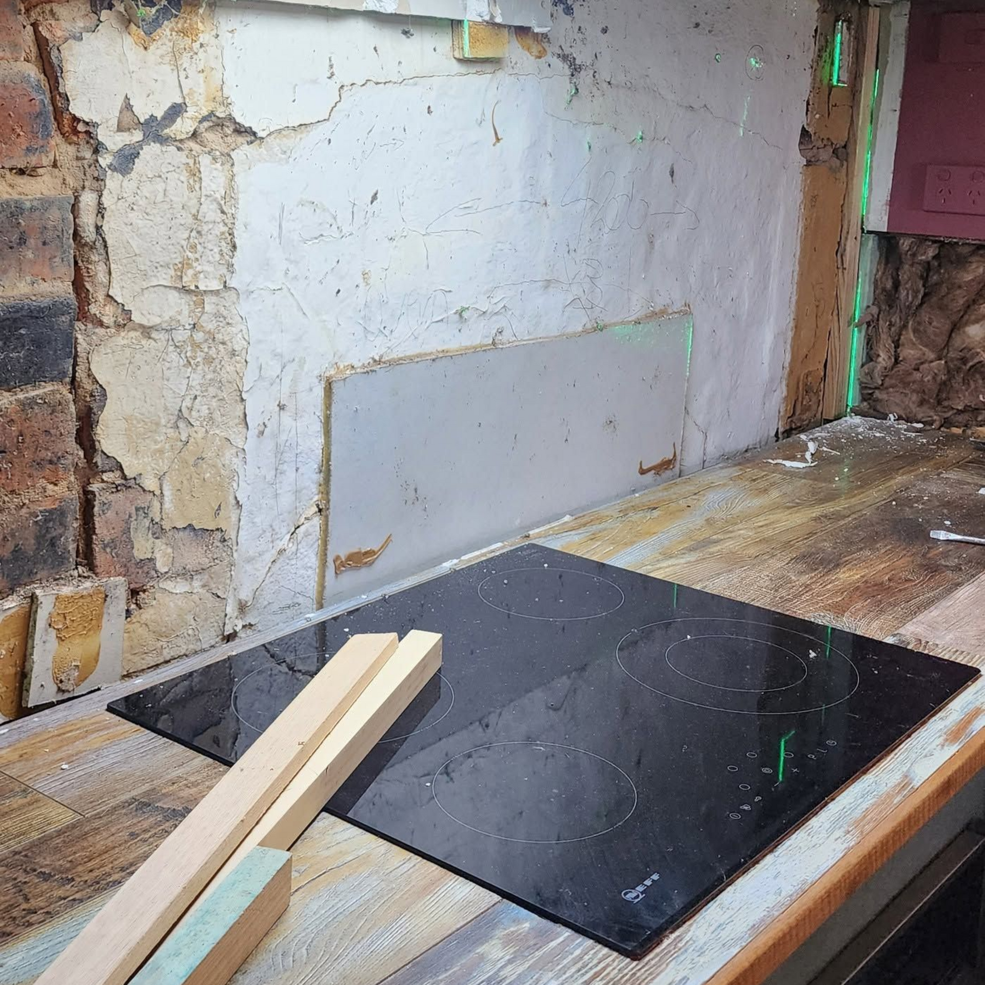 Partially renovated wall with exposed plaster and boards on a workbench, with a black tile panel in front