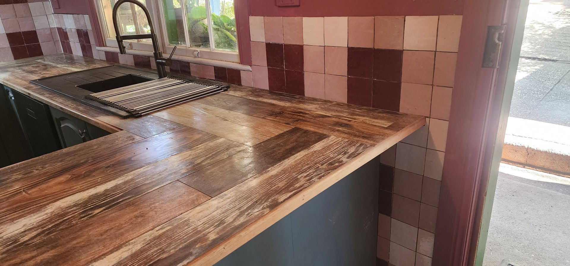 Rustic kitchen countertop with a sink, dark wood finish, and red-tiled backsplash by a window