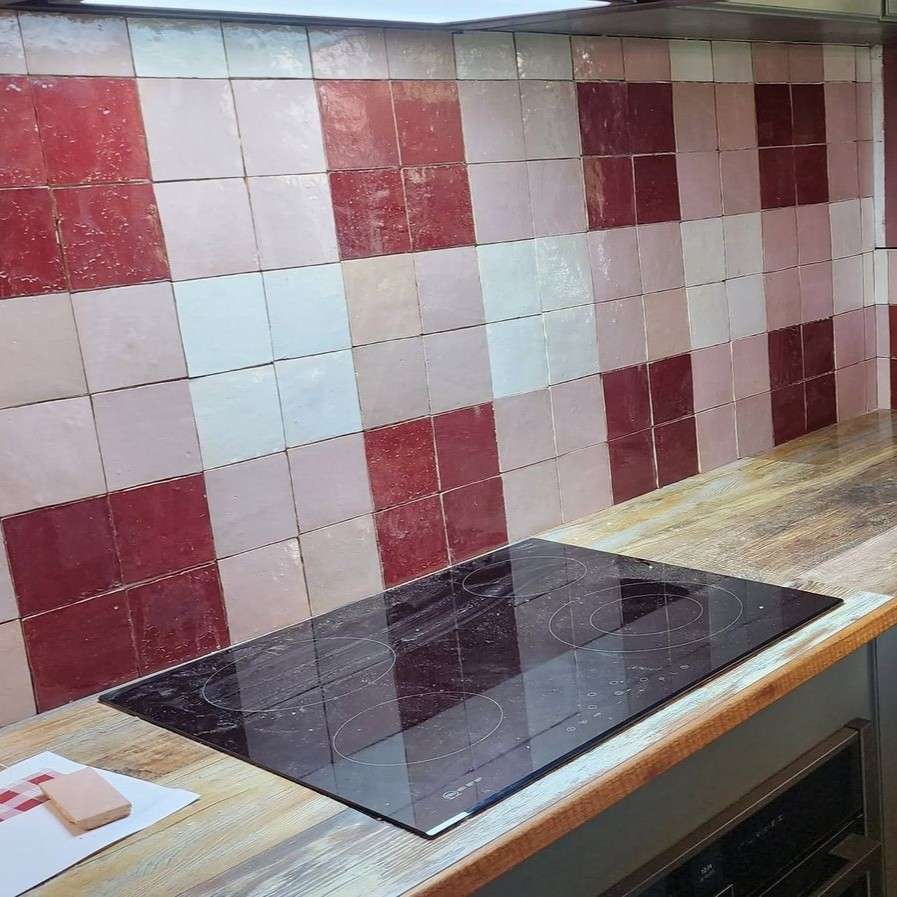 Kitchen countertop with black glass cooktop against a red-and-white tiled backsplash