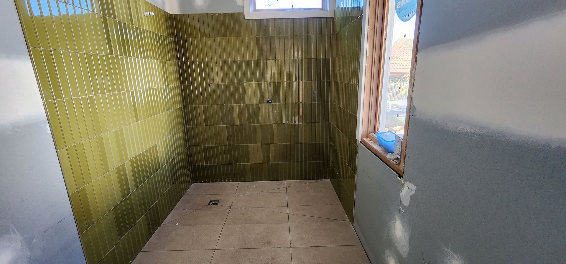 Small tiled room with green patterned walls, a blue wall, and a window on the right.