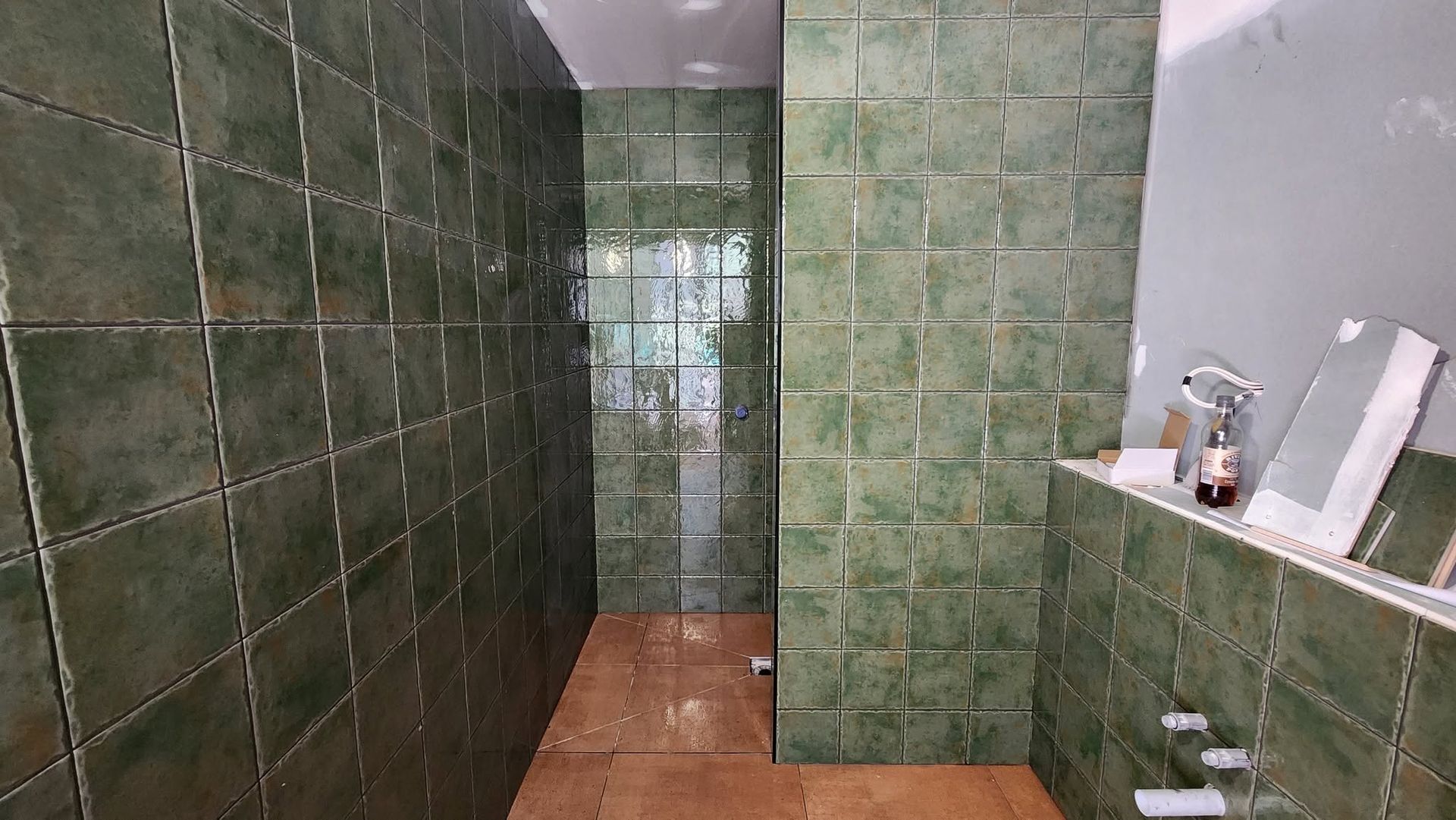 Narrow green-tiled bathroom with a shower stall and vanity area on the right.