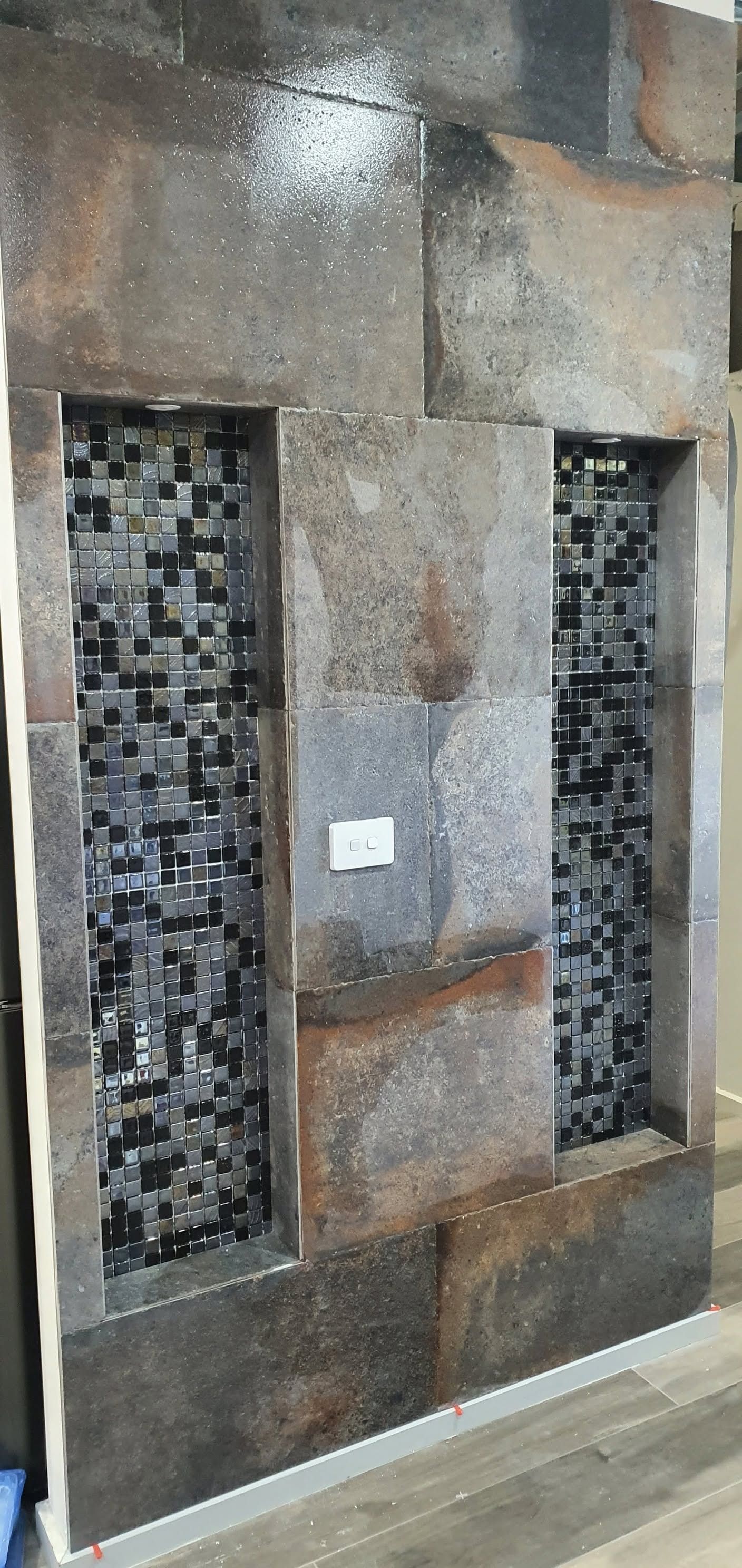 Two narrow mosaic wall panels between tan stone blocks in a tiled interior wall