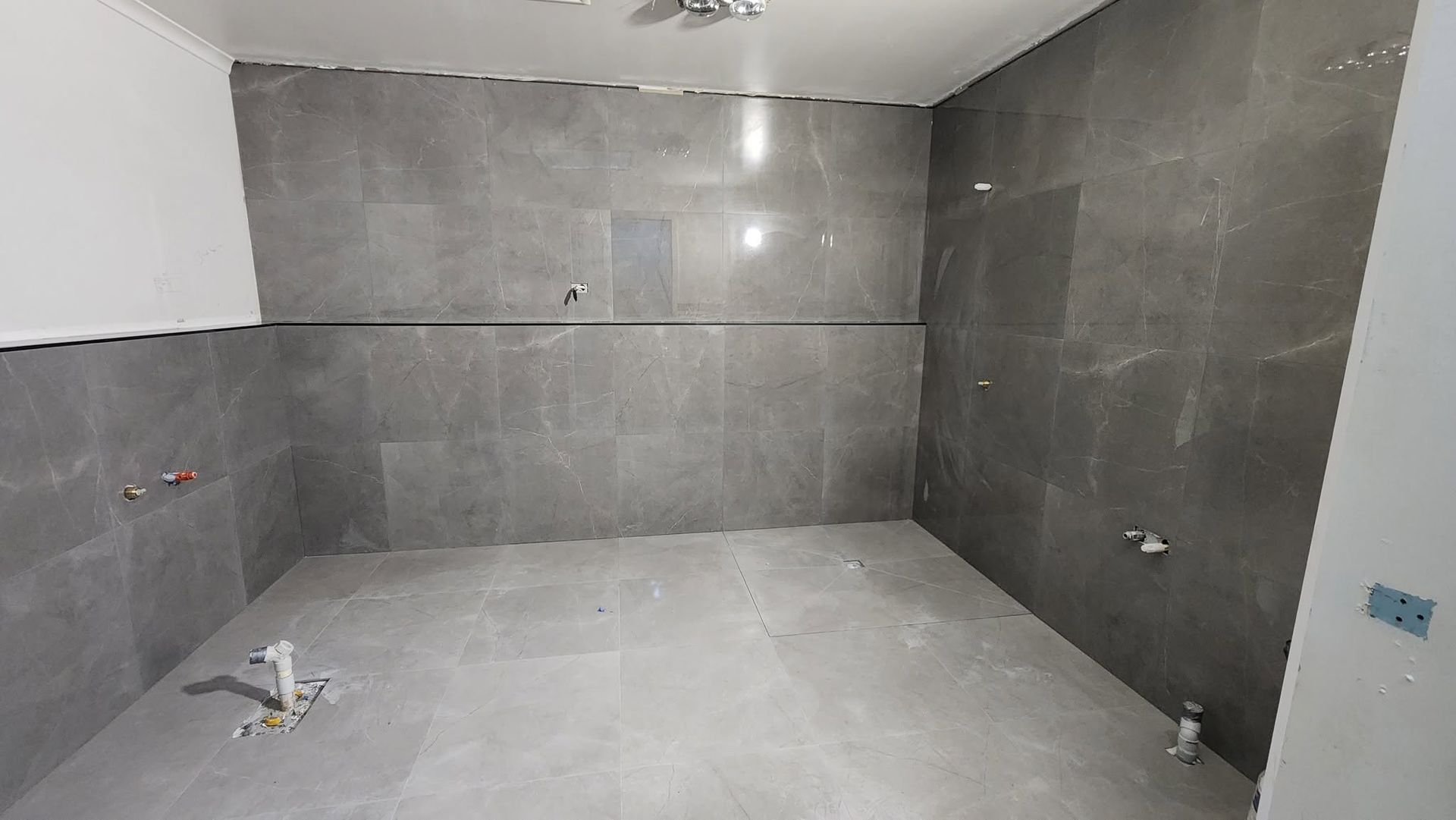 Empty tiled bathroom under construction with gray walls, floor, and fixtures
