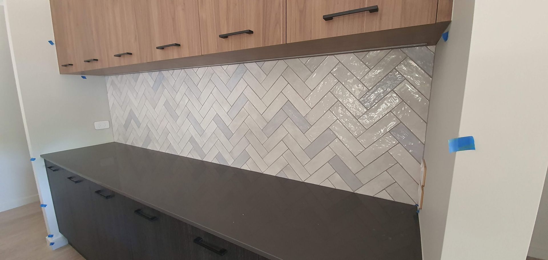 Kitchen with dark countertop, wood cabinets, and white herringbone tile backsplash