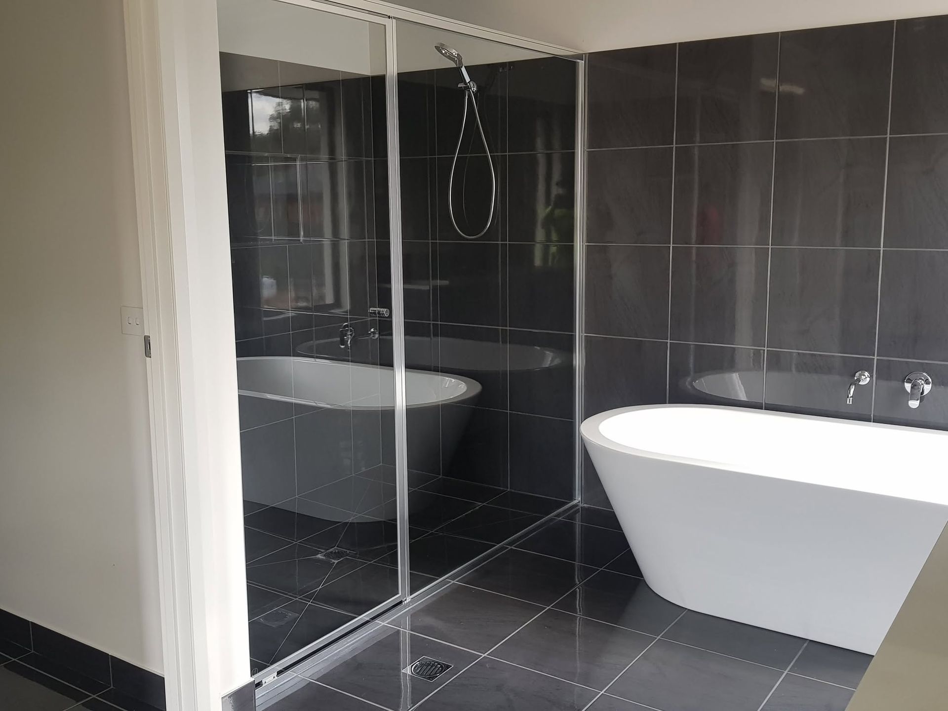 Modern bathroom with a freestanding white tub, black tiled shower, and glass partition