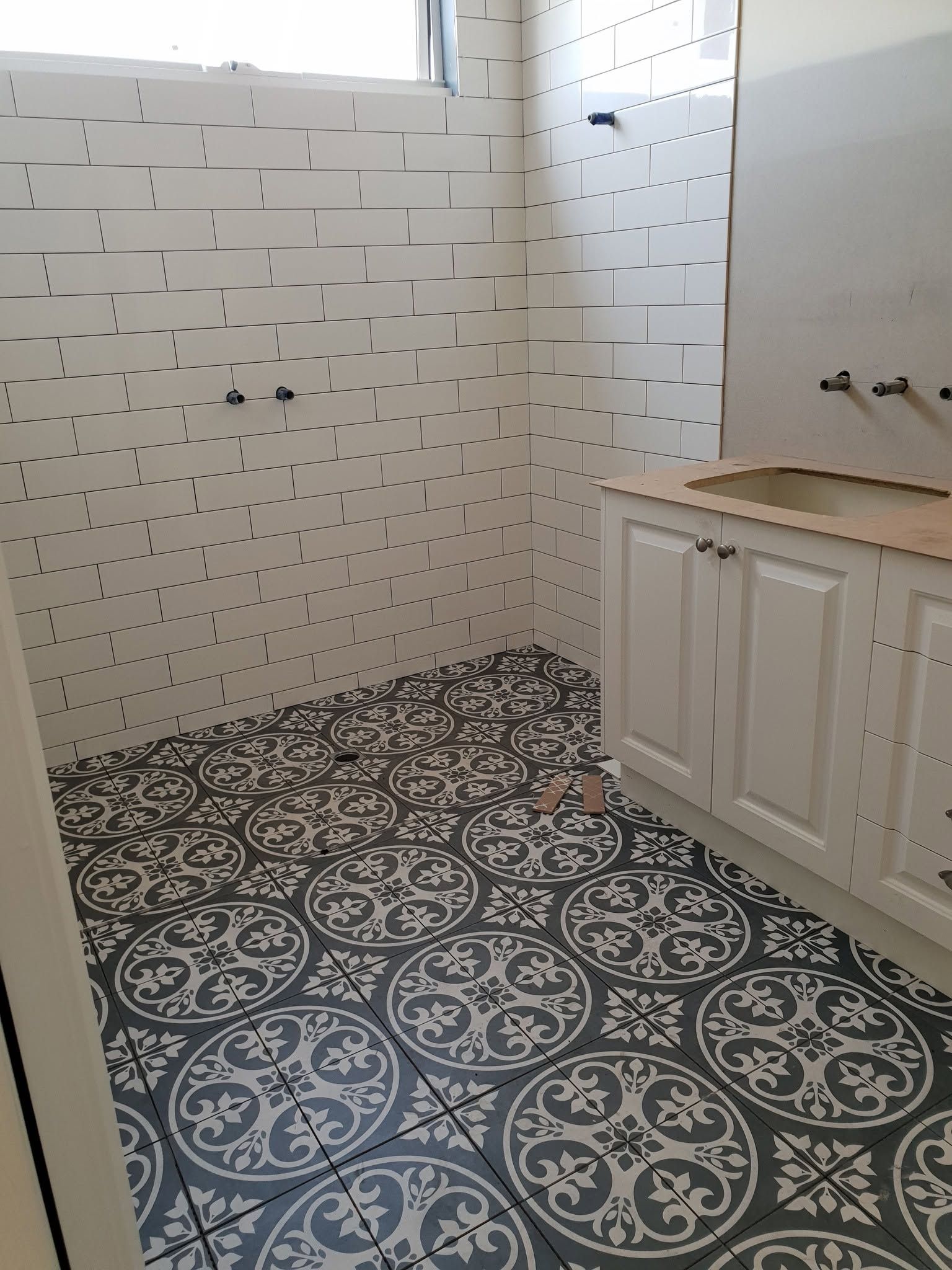 Small bathroom with patterned tile floor, white tiled walls, and a vanity cabinet under a window.