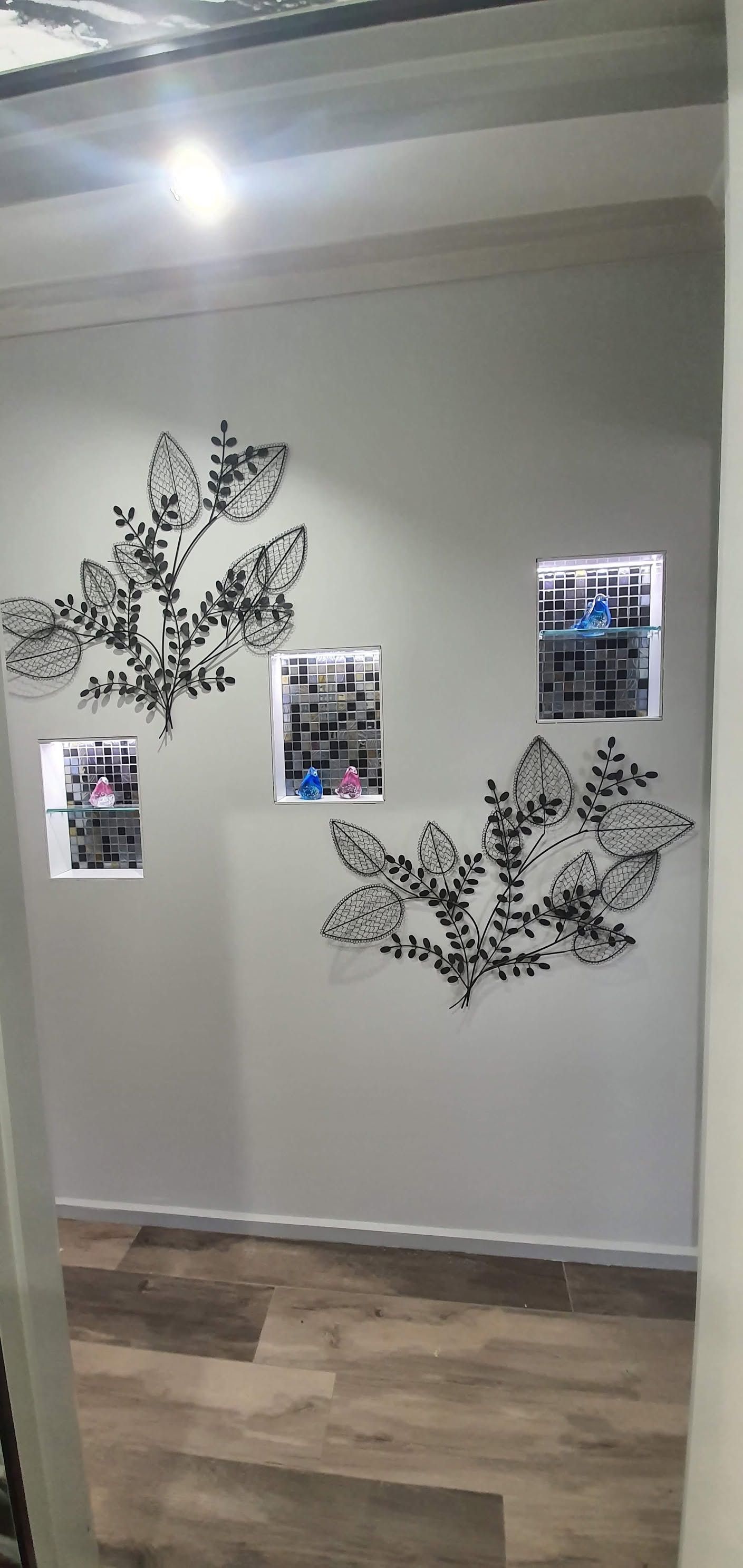 Gray wall with black leafy wall decals and three small framed photos above a wood floor