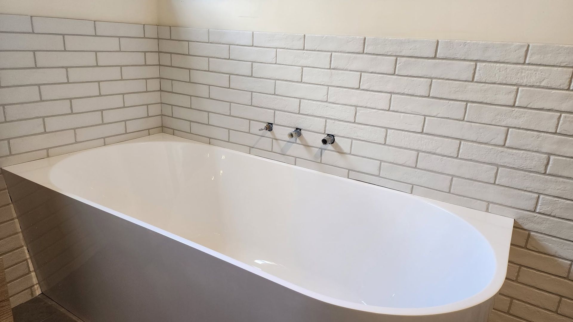 White freestanding bathtub against a white subway-tile wall in a bathroom