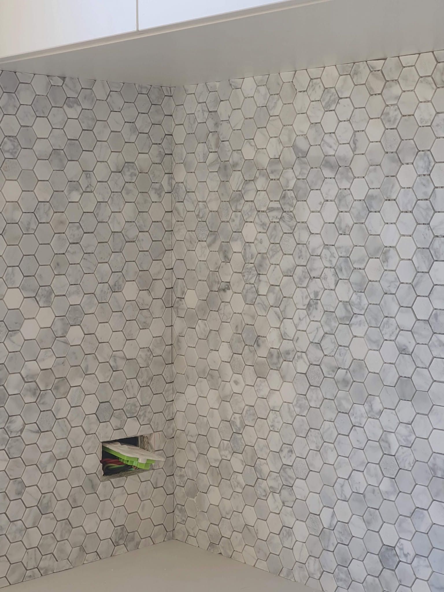 Tiled shower stall with hexagon-pattern wall tiles and a built-in niche holding a green item