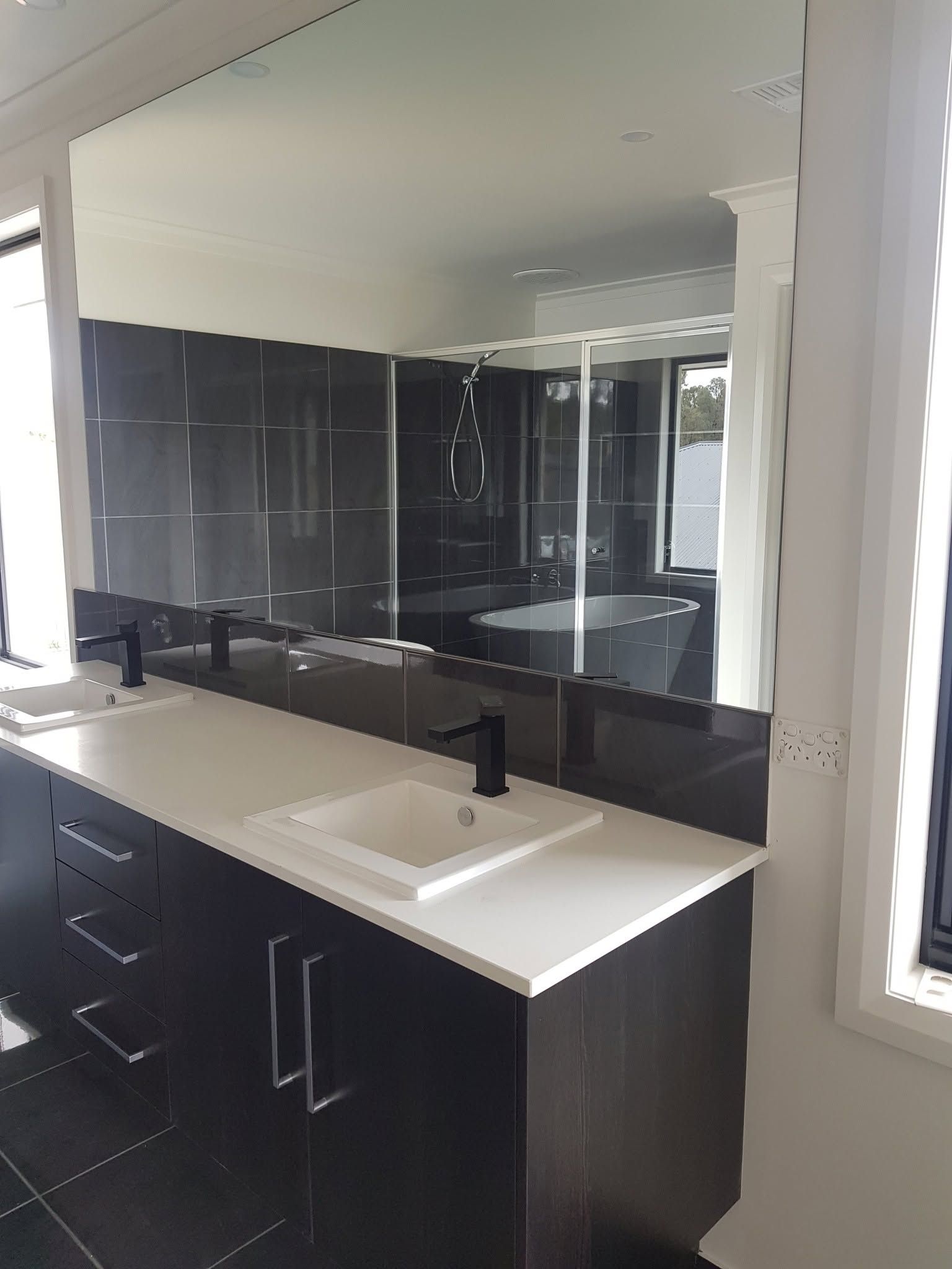 Modern bathroom with dark tile walls, black vanity, white countertop, and large mirror