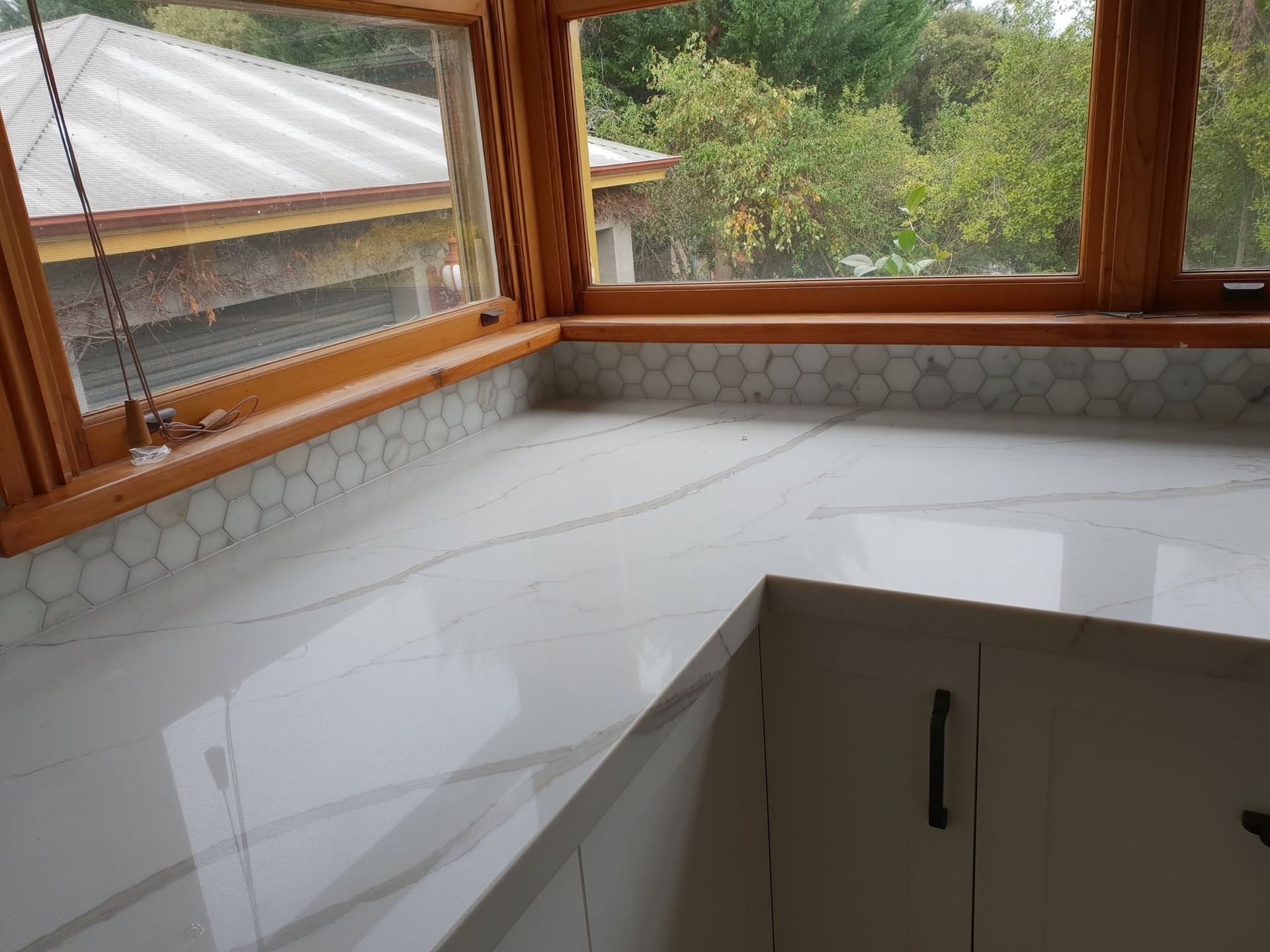 White marble kitchen countertop with a sink by large windows overlooking greenery