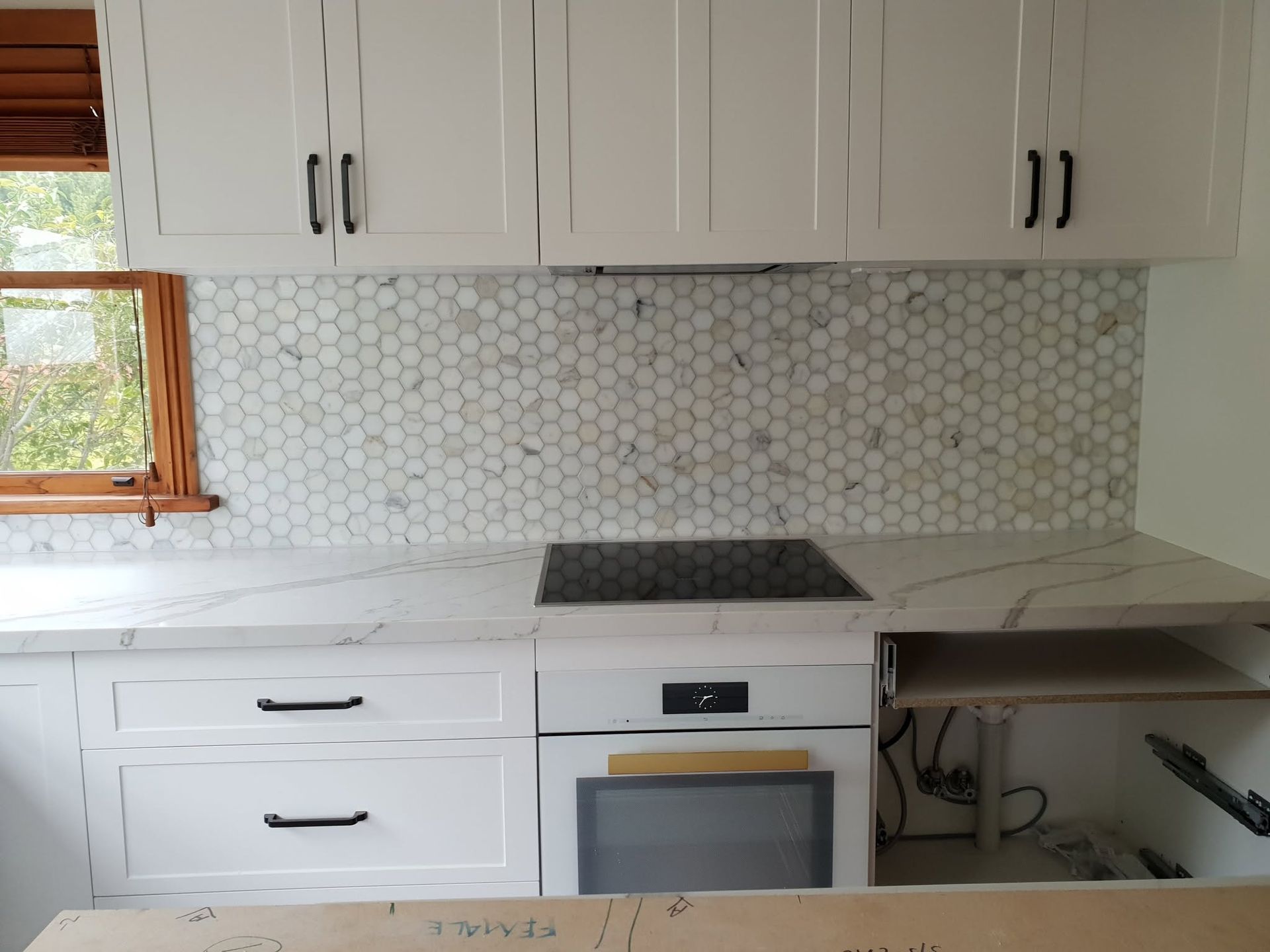 White kitchen with cabinets, hex tile backsplash, stovetop, and countertop by a window