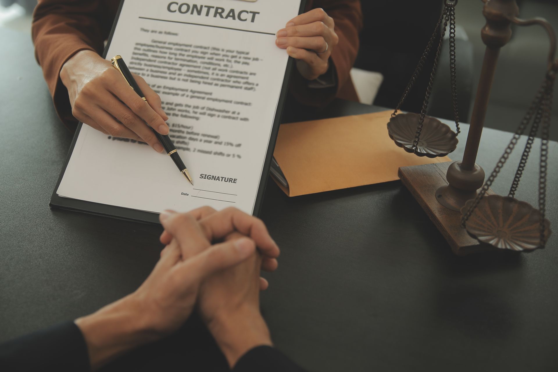 A person is signing a contract in front of a scale of justice.