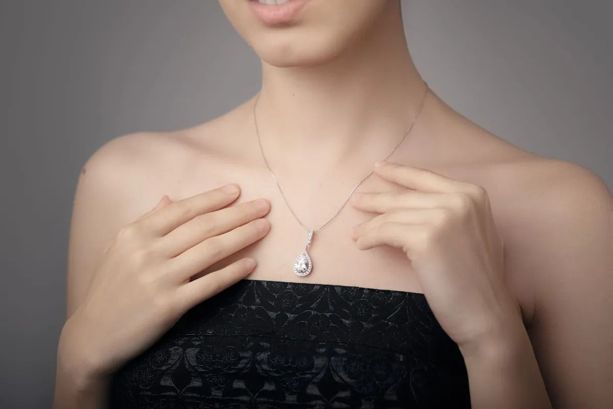 Una persona che indossa un top nero senza spalline si sistema una collana d'argento su uno sfondo grigio.