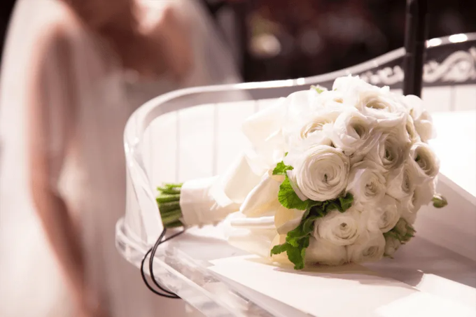 Bouquet da sposa bianco su una sedia, con rose bianche e dettagli in nastro verde.