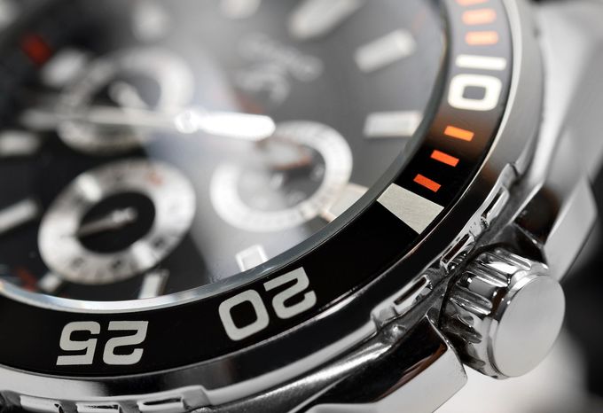 Primo piano di un orologio da polso analogico color argento con quadrante nero e dettagli arancioni.