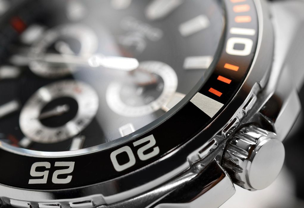 Primo piano di un orologio da polso analogico color argento con quadrante nero e dettagli arancioni.