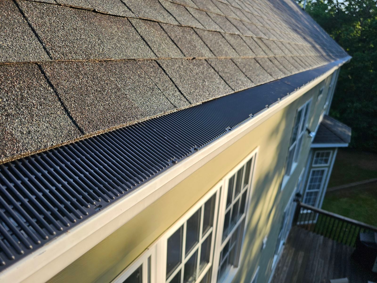 Gutter with a black guard on a house roof with gray shingles. White windows below.