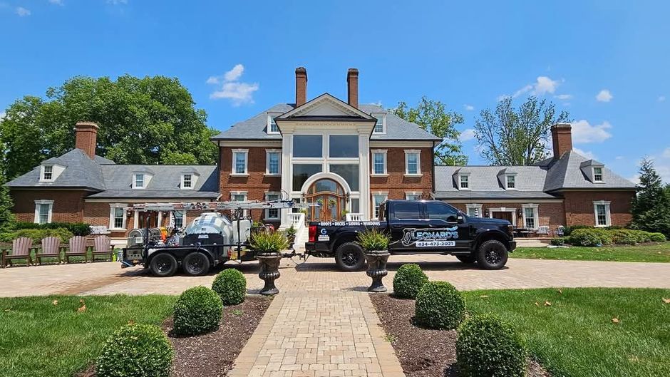 Brick mansion with two service trucks on a manicured lawn. Bright blue sky overhead.
