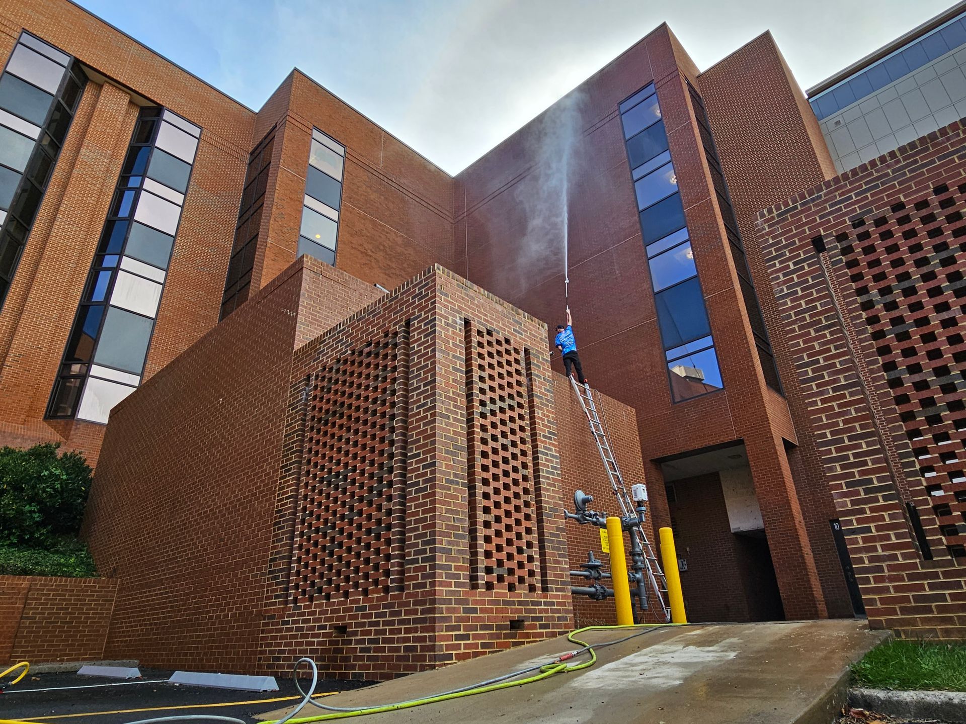 A person power washing the brick exterior of a building using a ladder.