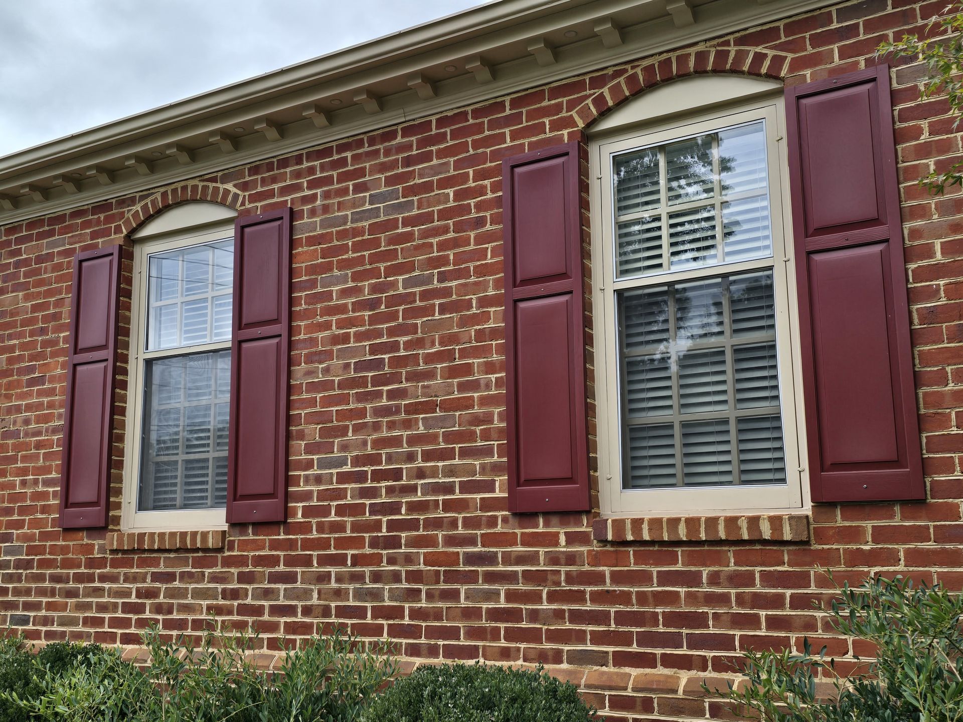 Red brick building with two arched windows and matching red shutters.