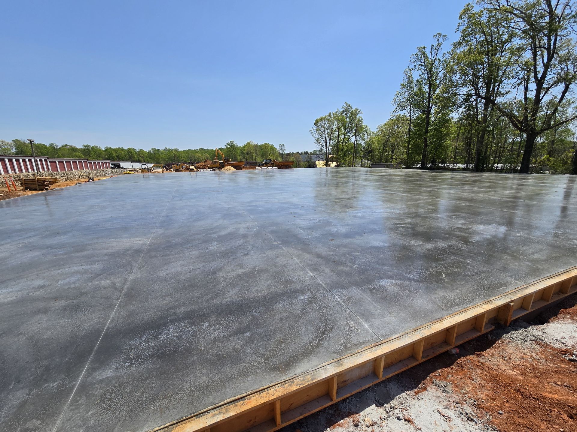 Freshly poured concrete slab on a construction site; clear sky, trees in the background.
