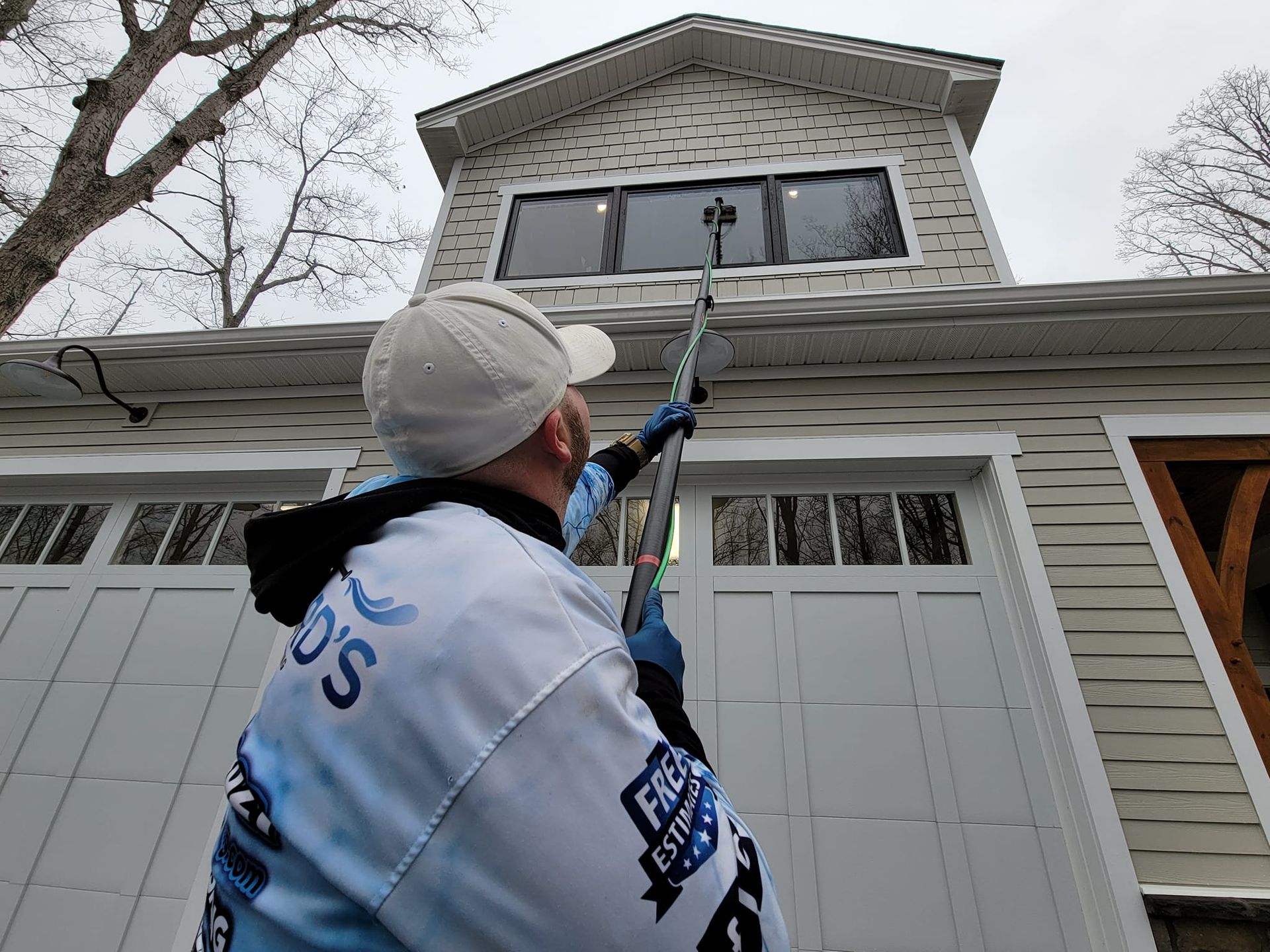 Man washing windows with a long-handled tool on a two-story house; cloudy sky.
