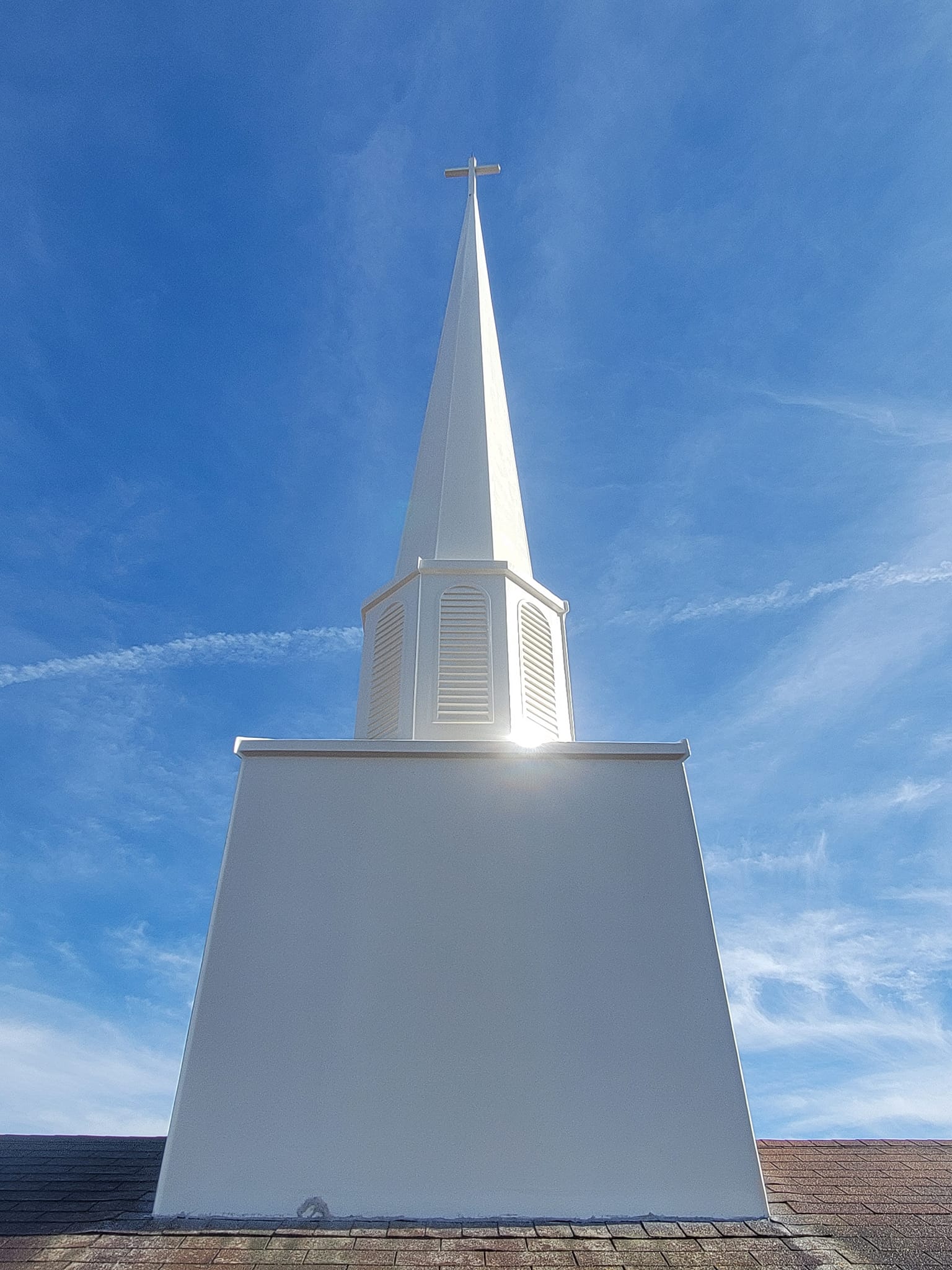 White church steeple against a blue sky, topped with a cross.