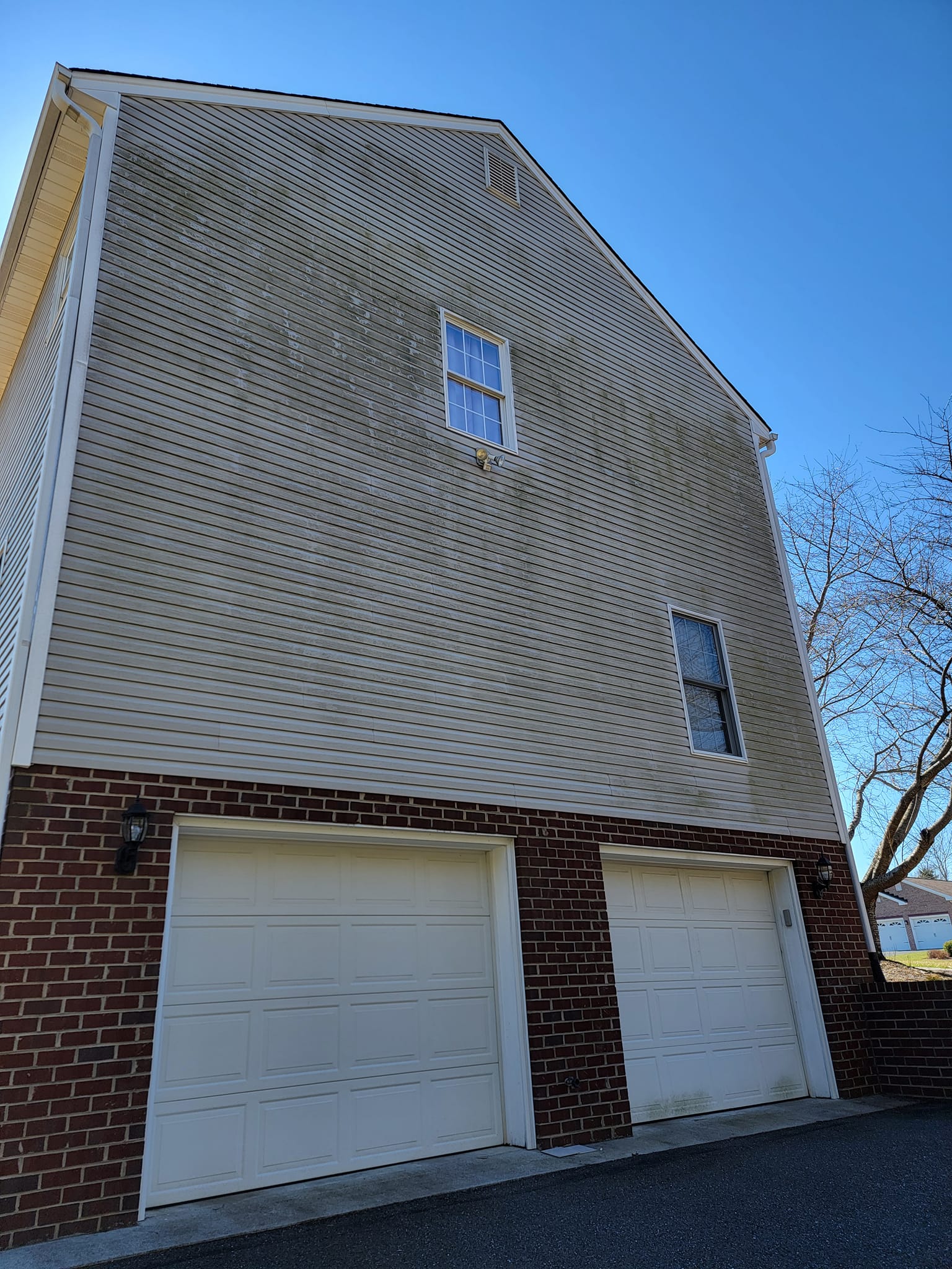 Two-story house with beige siding patterned in a spiral over two garage doors and brickwork, under a blue sky.