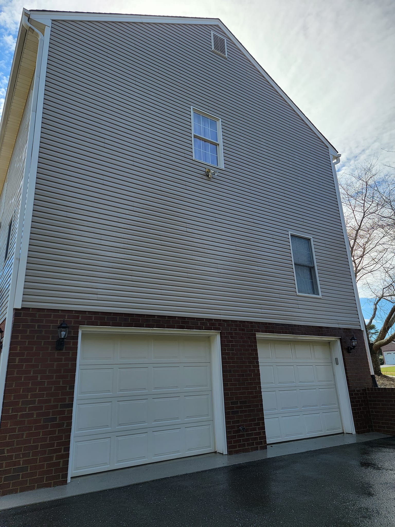 Two-story house with brick garage doors, siding, and windows against a cloudy sky.