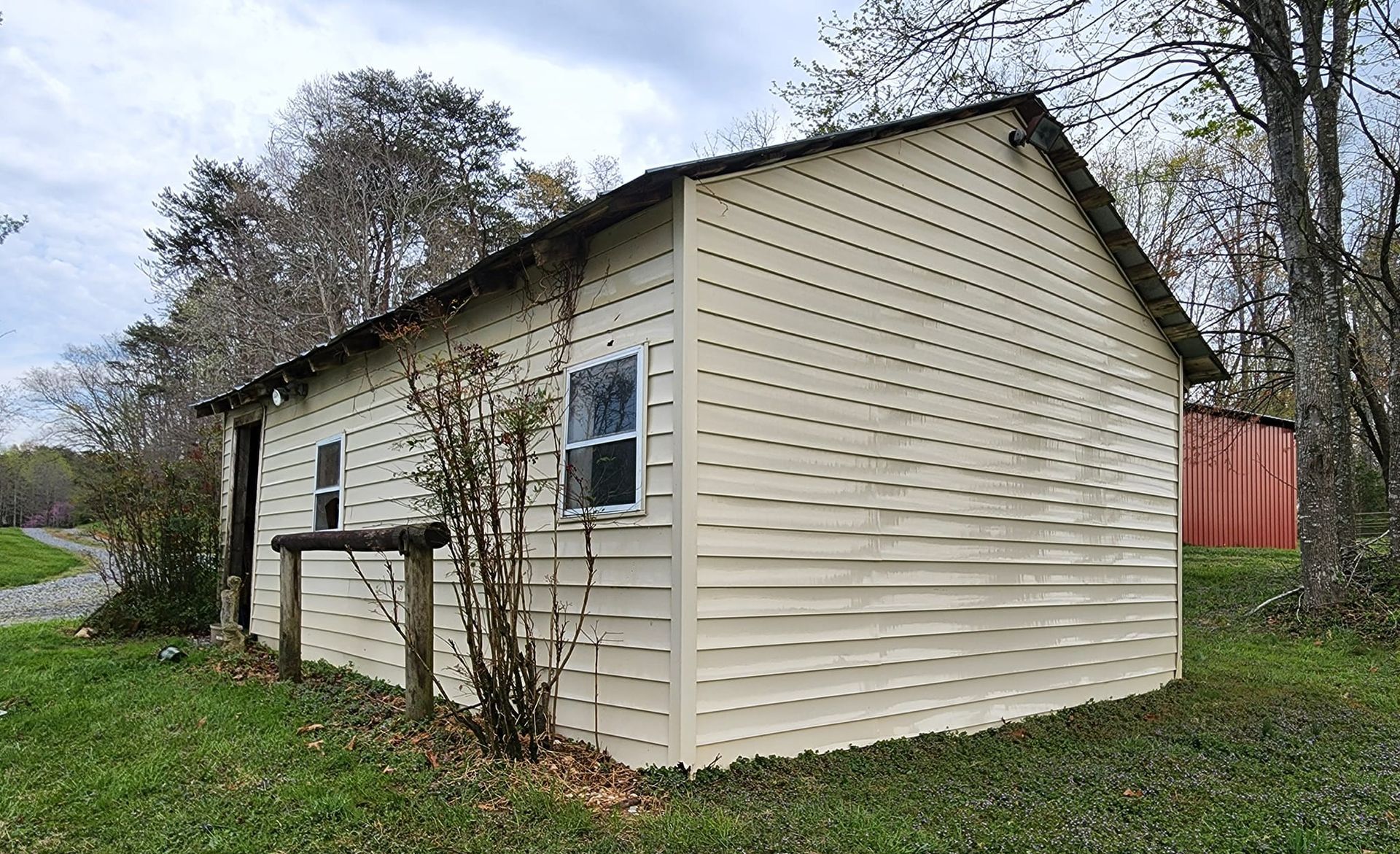 A weathered beige shed with a metal roof in a grassy area with trees.