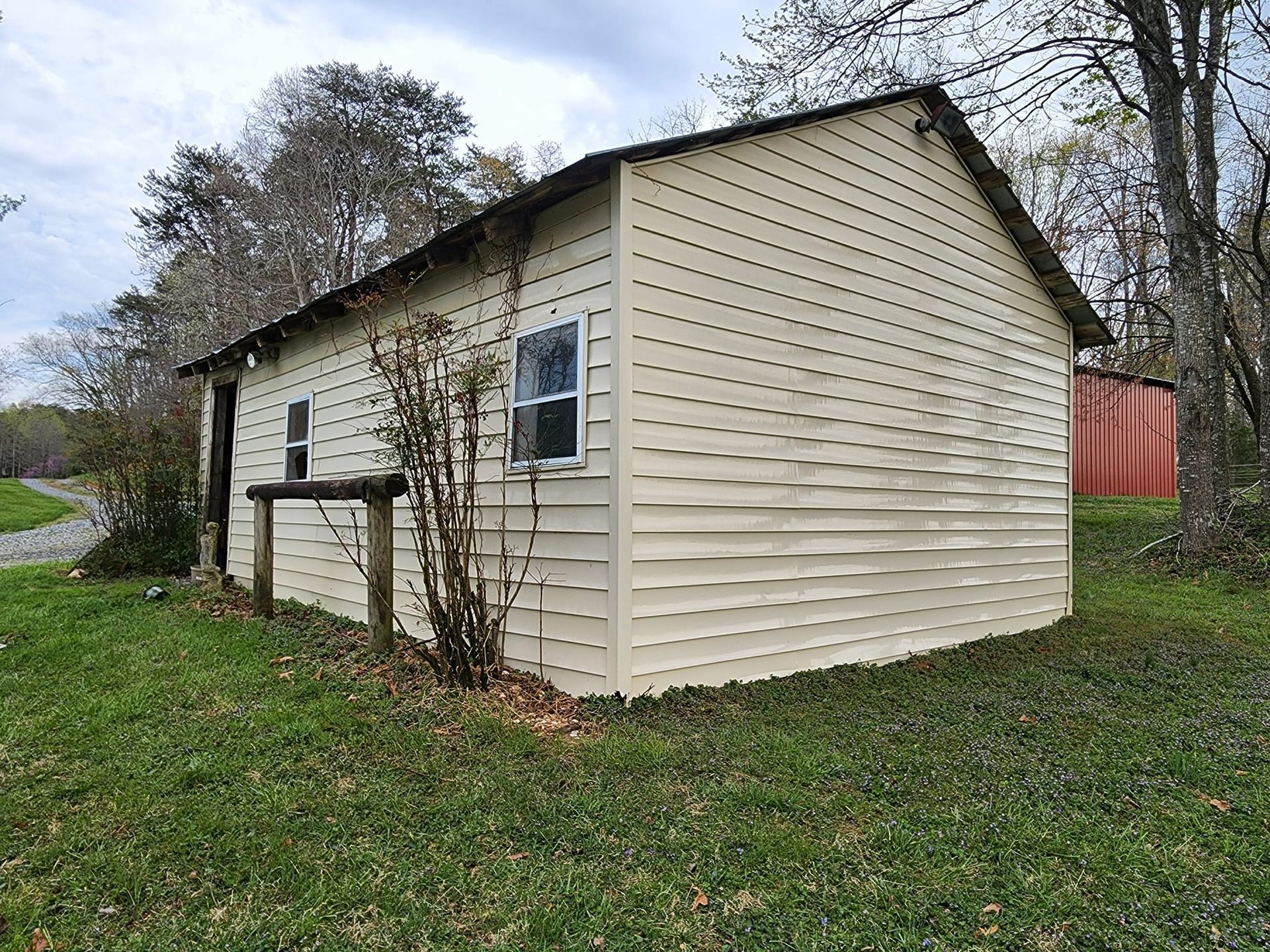 Tan building with a dark roof and two windows on a grassy area with trees.