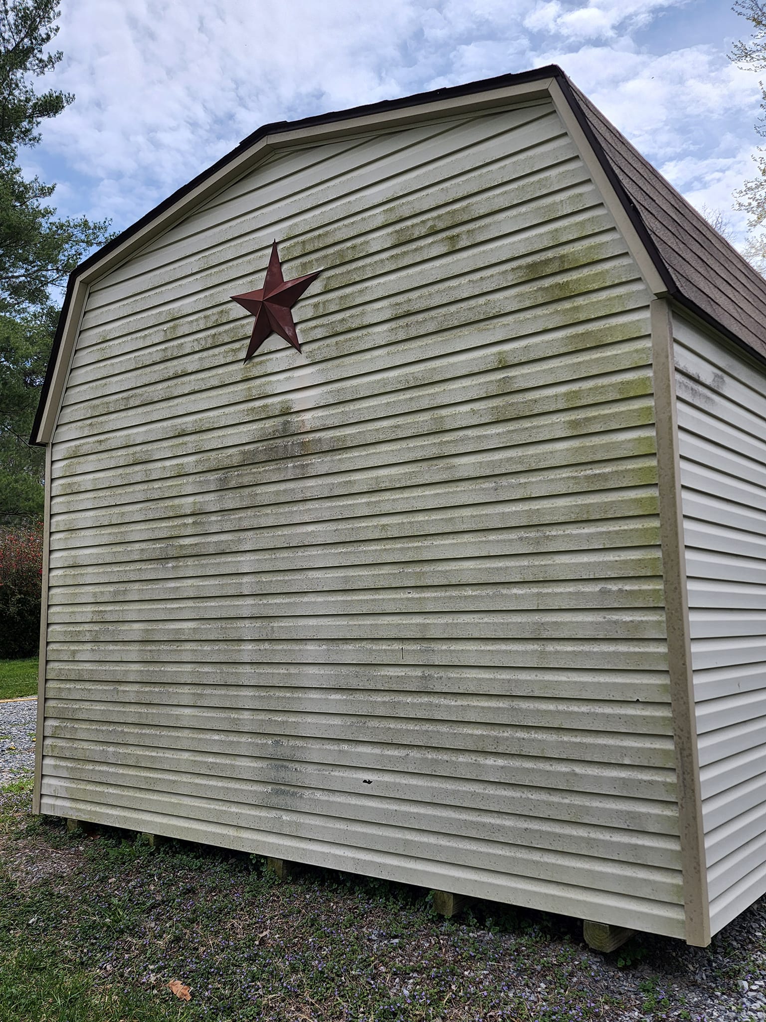 Tan shed with green algae, a red star, and a brown roof.