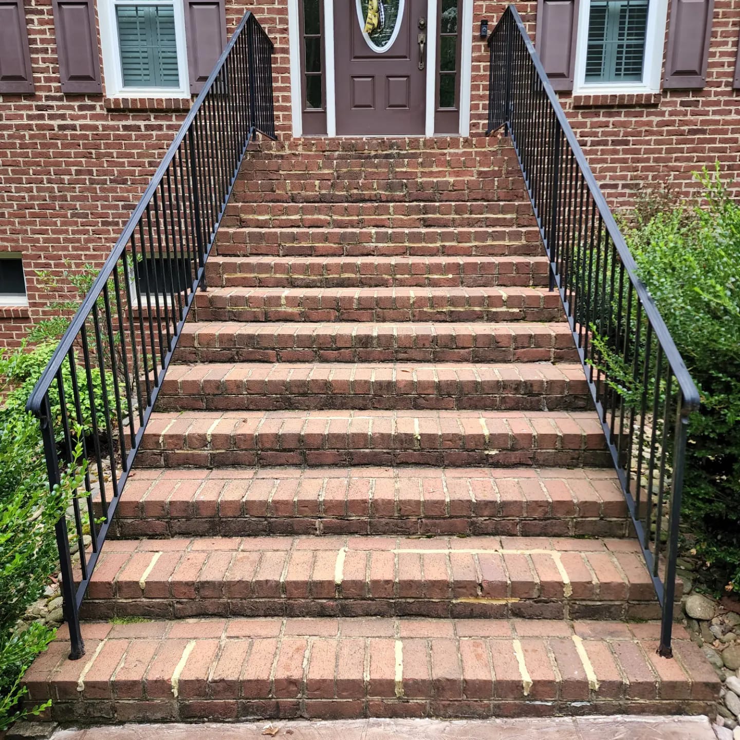 Brick steps leading up to a brown door, flanked by black metal railings, in front of a brick building.