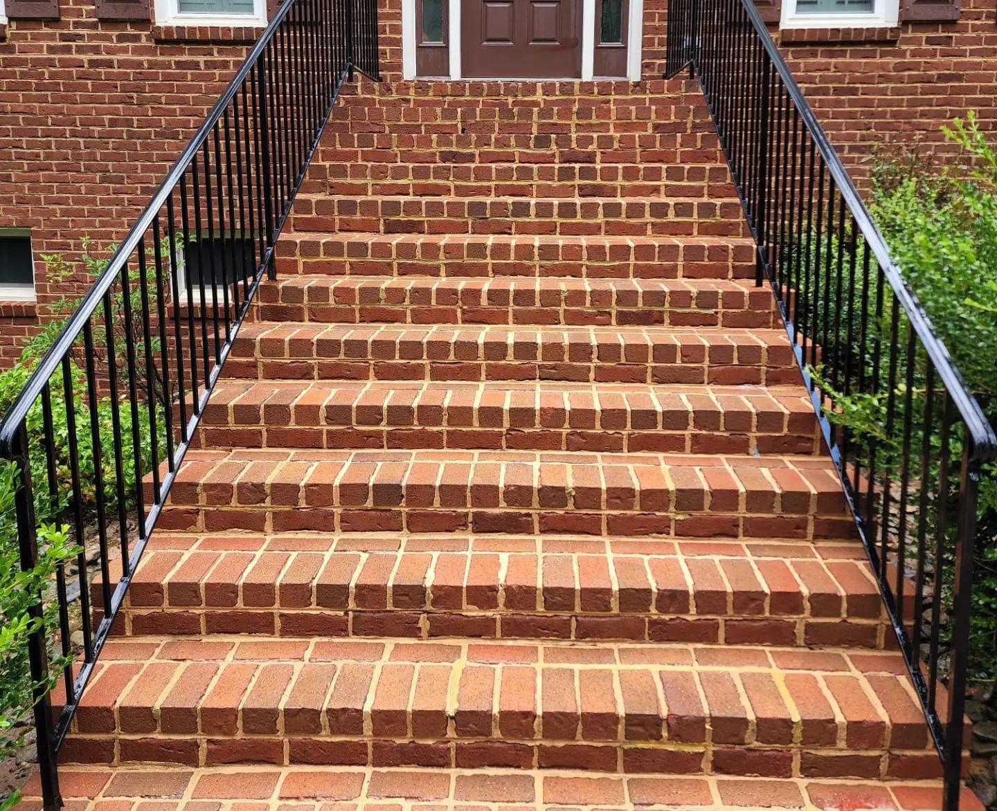 Brick steps leading up to a brown door; black metal railings on either side.