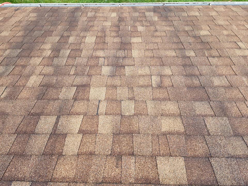 Brown asphalt shingle roof, showing variation in color and texture, set against a bright, outdoor sky.