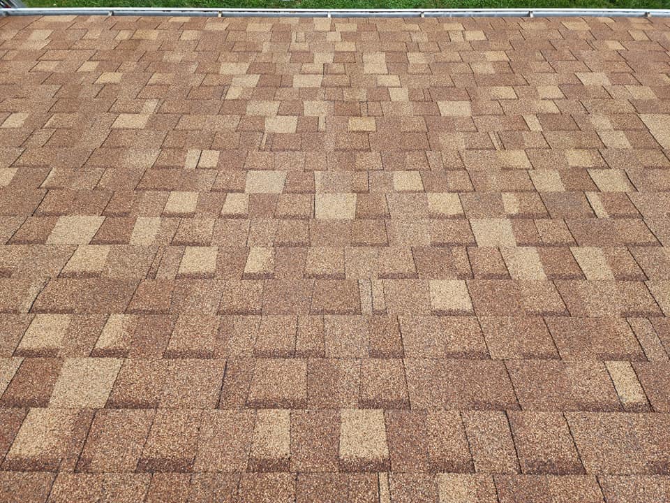 Brown and tan asphalt shingle roof with a textured pattern, angled slightly from above.