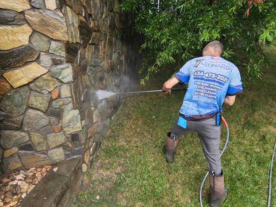 Man power washing a stone wall outside, wearing work attire.
